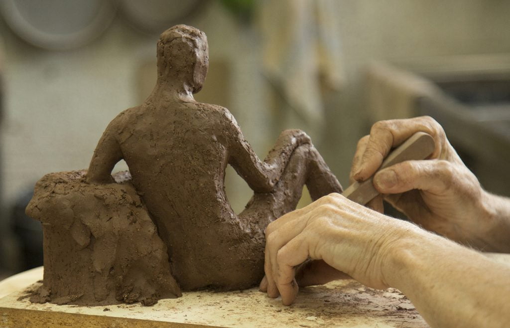 Hands sculpting red clay figure